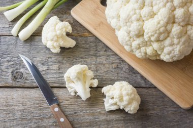 Taze organik karnabahar, ahşap zemin üzerine yeşil soğan ve bıçak ile parçalar halinde kesilmiş.