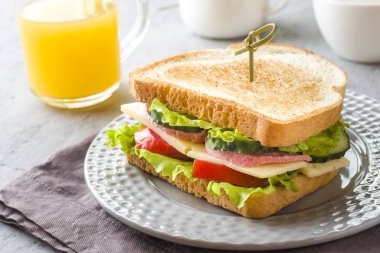 Peynir, jambon ve bir plaka üzerinde taze sebze ile sandviç. Taze meyve suyu ve bir fincan kahve. Kahvaltı kavramı
