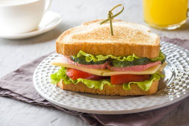 Peynir, jambon ve bir plaka üzerinde taze sebze ile sandviç. Taze meyve suyu ve bir fincan kahve. Kahvaltı kavramı