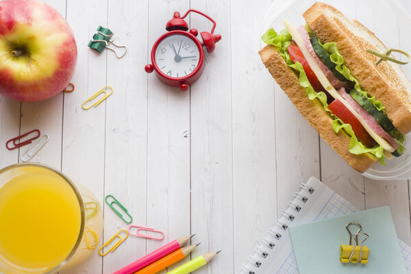 Закуска для школы со сэндвичем, свежим яблочным и апельсиновым соком. Красочные школьные принадлежности. Копирование пространства
