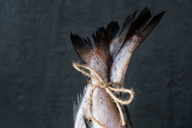 Raw fish tails tied with rope with bow on dark background. Selective focus. clipart