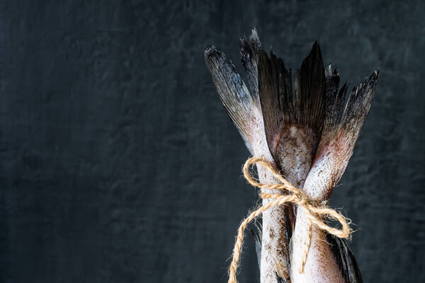 Raw fish tails tied with rope with bow on dark background. Selective focus.
