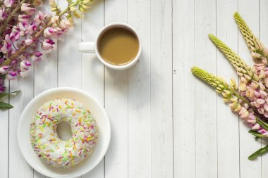 Bir fincan kahve ve acı bakla çiçek çörek üzerinde ahşap masa lambası ile natürmort.
