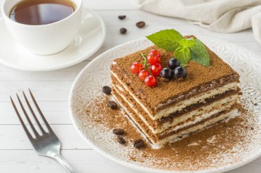 Taze meyveleri ve açık renkli bir tabağa nane ile leziz Tiramisu pasta. Bir fincan kahve ile kahvaltı