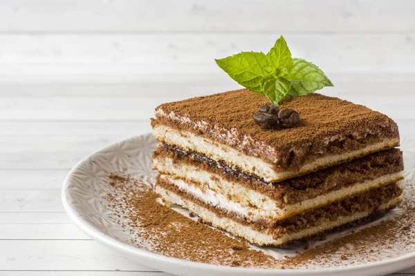 Kahve çekirdekleri ve açık renkli bir tabağa üzerinde taze nane ile leziz Tiramisu pasta.