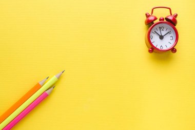 Parlak renkli kalemler ve sarı zemin üzerine çalar saat