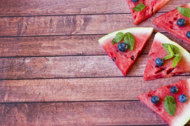 Rustik koyu arka plan üzerinde bir yaban mersini ve nane ile dilimlenmiş karpuz parçalar. Yaz konsepti.