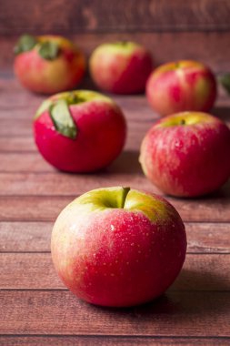 Koyu ahşap zemin üzerine yeşil yaprakları ile taze kırmızı elmalar