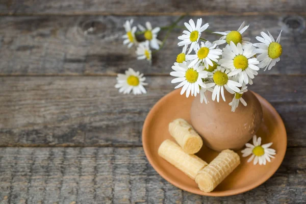 Still life of a bouquet of daisies in a vase and waffle tubes. Wooden rustic style