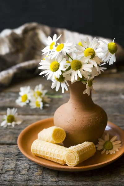 Still life of a bouquet of daisies in a vase and waffle tubes. Wooden rustic style