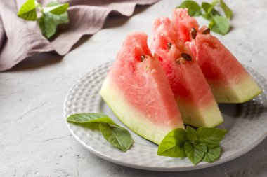 Ahşap bir zemin üzerine nane yaprakları ile bir tabağa dilimlenmiş karpuz.