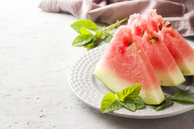 Ahşap bir zemin üzerine nane yaprakları ile bir tabağa dilimlenmiş karpuz.