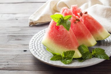 Ahşap bir zemin üzerine nane yaprakları ile bir tabağa dilimlenmiş karpuz.