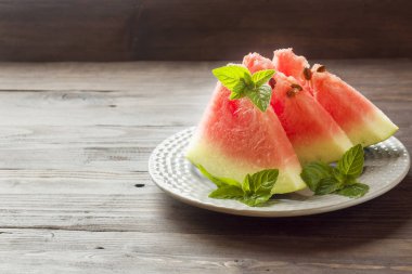 Ahşap bir zemin üzerine nane yaprakları ile bir tabağa dilimlenmiş karpuz.