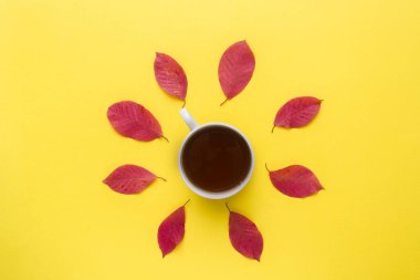 Kırmızı sonbahar yaprakları ve bir fincan kahve parlak sarı bir arka plan üzerinde. Sonbaharın soyut kavram.