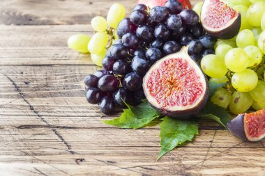 Taze sonbahar meyve natürmort. Üzüm siyah ve yeşil, incir ve kopya alanı ile ahşap bir masa yapraklarda