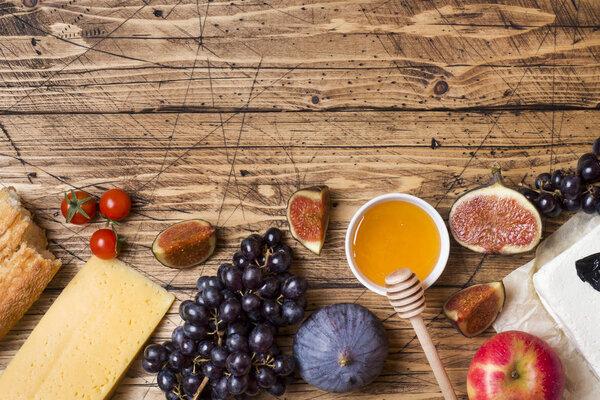 Cheese, wine, baguette grapes figs honey and snacks on the rustic wooden table top with copy space