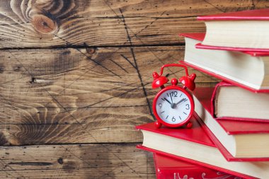 Bir yığın ciltli kitap ve ahşap bir masa üzerinde bir çalar saat. Metin için yer kopyalayın.