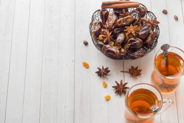 Oryantal tatlılar, kurutulmuş meyve tarihleri ve kuru üzüm, tarçın ve anasonu bir tabak içinde. Ahşap arka plan üzerinde bardaklarda Türk çayı