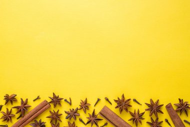 Yıldız anason, tarçın ve karanfil sarı bir arka plan üzerinde bileşimi. Soyut düz desen, üstten görünüm.