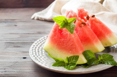 Ahşap bir zemin üzerine nane yaprakları ile bir tabağa dilimlenmiş karpuz.
