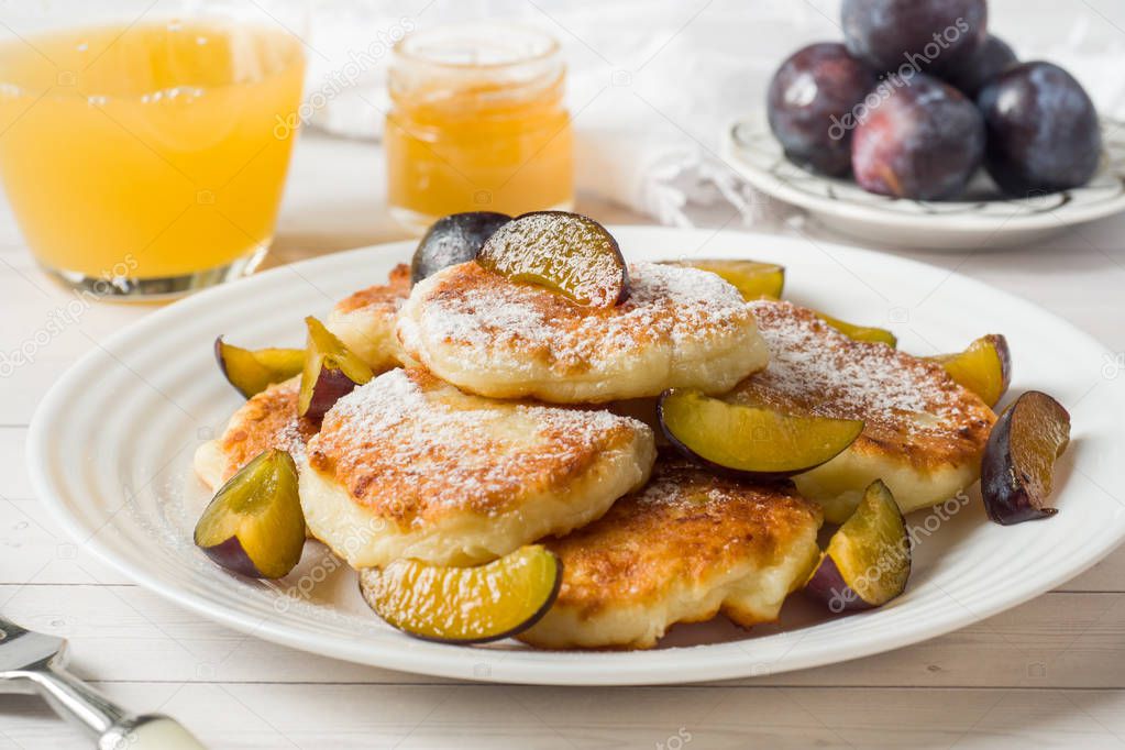 Cheese pancakes in powdered sugar with fresh plums on a plate.