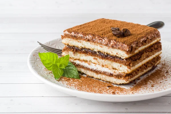 Kahve çekirdekleri ve açık renkli bir tabağa üzerinde taze nane ile leziz Tiramisu pasta.