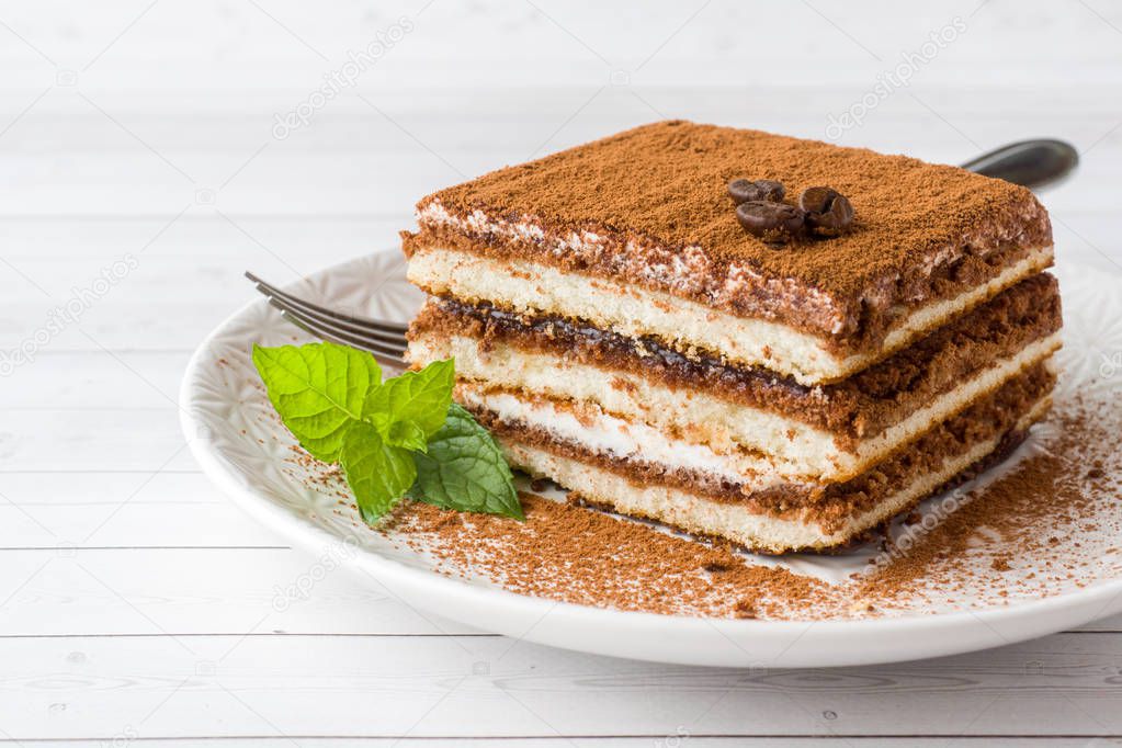 Delicious Tiramisu cake with coffee beans and fresh mint on a plate on a light background.