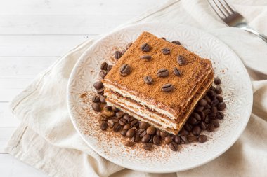 Açık renkli bir tabağa üzerinde kahve çekirdekleri ile leziz Tiramisu pasta.