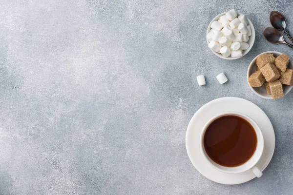 Cup of hot chocolate, brown sugar and marshmallow on grey table with copy space.