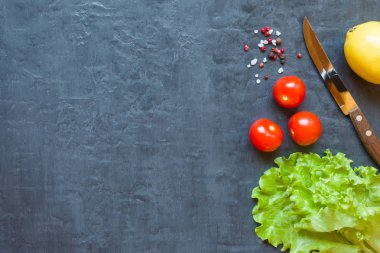 Taze yeşil marul yaprağı, cherry domates, limon ve baharat koyu arka plan üzerinde.