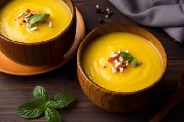 Karanlık kurullarında ahşap kase içinde baharatlar ile püre kabak çorbası