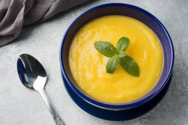 Masanın üzerinde mavi bir tabak içinde baharatlar ile püre kabak çorbası