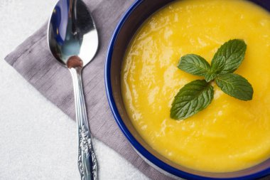 Masanın üzerinde mavi bir tabak içinde baharatlar ile püre kabak çorbası