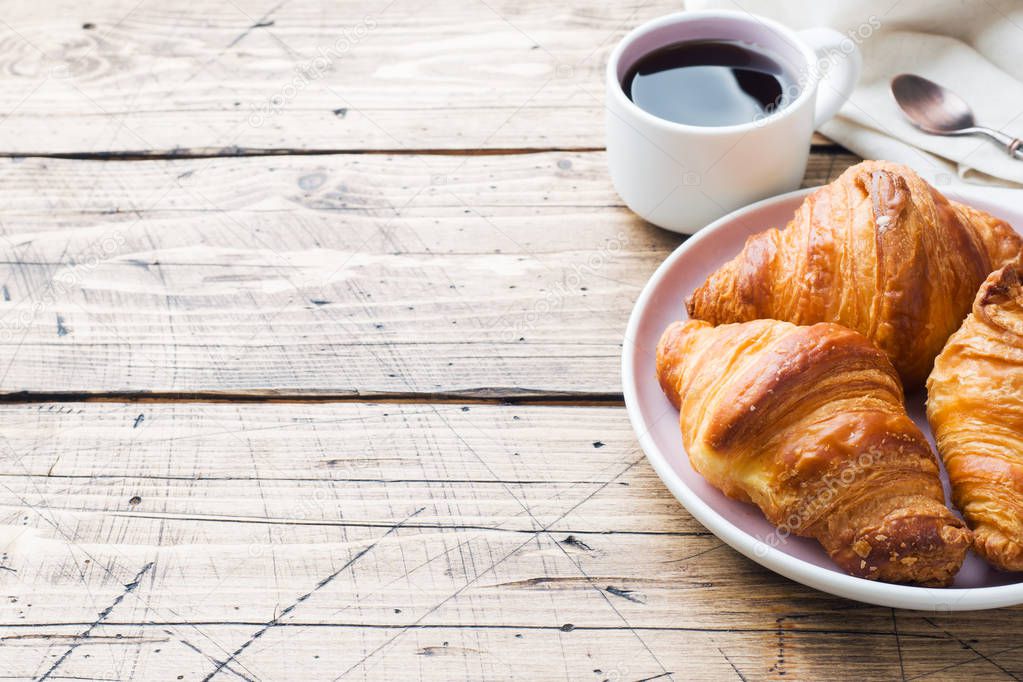 Breakfast croissants on a plate and a Cup of coffee, wooden background, copy space