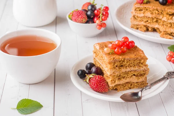 Tatlım kek çilek, nane ve Frenk üzümü, bir fincan çay hafif bir arka plan üzerinde.