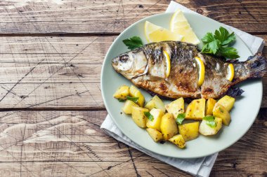 Fırında Balık sazan limon yeşillik ve patates bir plaka üzerinde. Ahşap arka plan kopya alanı