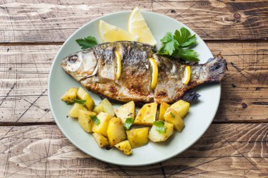 Fırında Balık sazan limon yeşillik ve patates bir plaka üzerinde. Ahşap arka plan