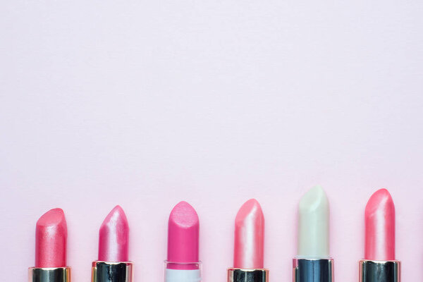 Set of colored pink lipsticks on pink background. Women's cosmetics. Selective focus. Copy space
