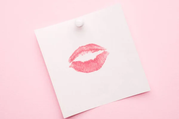 A lipstick kiss print on a piece of paper. Pink pastel background