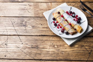 Tüp çikolatalı krep ve bir plaka üzerinde meyveleri. Ahşap arka plan. Kopya alanı