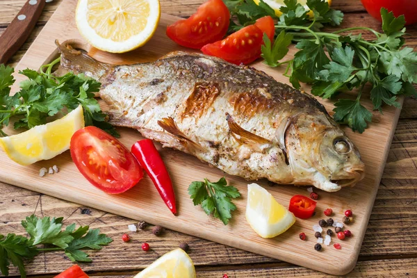 Pește de crap copt cu legume și condimente pe o masă de lemn . — Fotografie, imagine de stoc