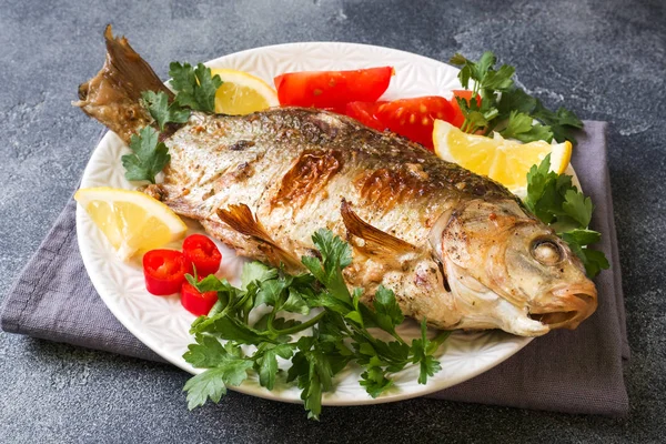 Gebakken karper vis met groenten en kruiden op een plaat op een donkere tafel met een kopie van de ruimte. — Stockfoto