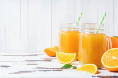 Cam Kavanoz ve Beyaz ahşap rustik zemin üzerine taze portakal portakal suyu.