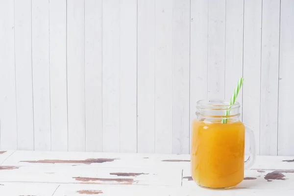 Sumo de laranja em frascos de vidro e laranjas frescas em um fundo rústico de madeira branca . — Fotografia de Stock