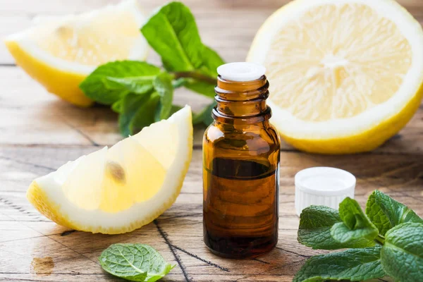 Alapvető citrom olaj, palack, friss gyümölcs szelet fa háttér. Természetes illatok. — Stock Fotó