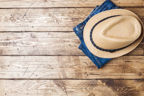 Summer women\'s clothes. Flat lay fashion photo. Blue jeans and sun hat on wooden background. Copy space