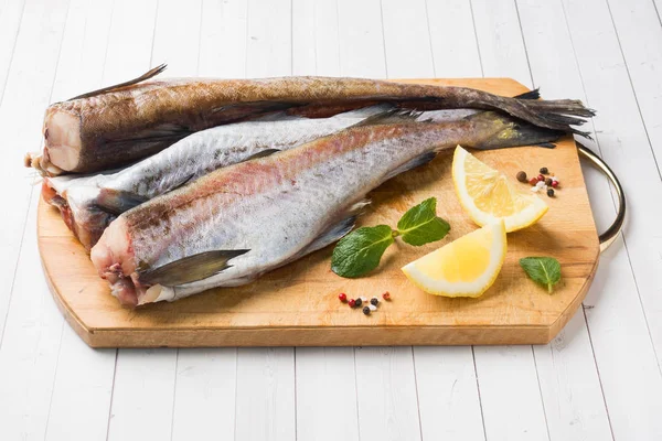 Pescado pollock fresco crudo en una tabla de madera con limón —  Fotos de Stock