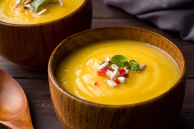 Karanlık kurullarında ahşap kase içinde baharatlar ile püre kabak çorbası.