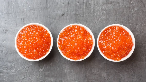 Red salmon caviar in a plate on a dark table. — Stock Photo, Image